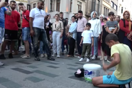 boy plays drum on yogurt bucket on street
