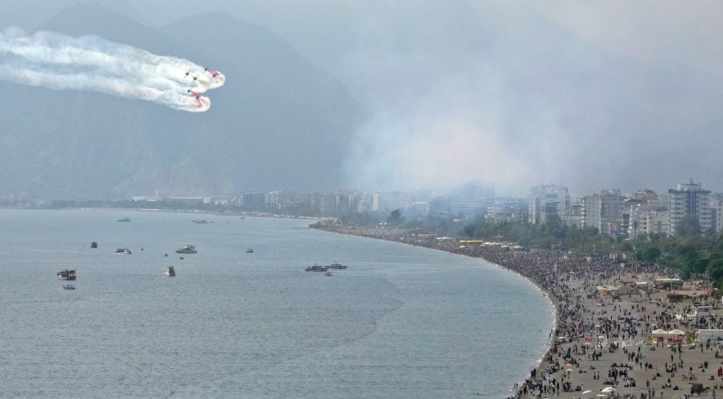 TÜRK YILDIZLARI ANTALYA'YI YAZA ÇEVİRDİ: BİNLERCE KİŞİ SAHİLİ DOLDURDU GÖKYÜZÜNE 100 ÇİZEREK GÖSTERİYE BAŞLAYAN TÜRK YILDIZLARI'NI VATANDAŞLAR VE TURİSTLER HEYECANLA İZLEDİ FALEZLERDE TOPLANAN KALABALIKTAN BAZILARI, GÖSTERİYİ DAHA İYİ İZLEYEBİLMEK İÇİN ÇİTLERİ AŞTI OĞLUYLA GÖSTERİYİ İZLEYEN VATANDAŞ: "GURUR VERİCİ"